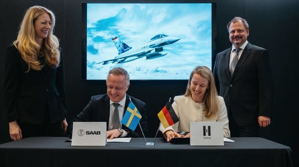 Representatives from Saab and Helsing sign an agreement at a table with Swedish and German flags, backed by a screen displaying a fighter jet.